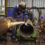 Male worker grinding use electric wheel grinding pipe sparks inside industrial construction.