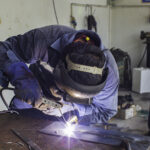 Welding male worker metal is part in machinery repair garage